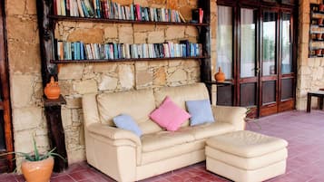 Un sofá de cuero color beige con cojines, una pared de piedra y una estantería llena de libros.