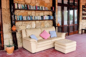 Un sofá de cuero color beige con cojines, una pared de piedra y una estantería llena de libros.