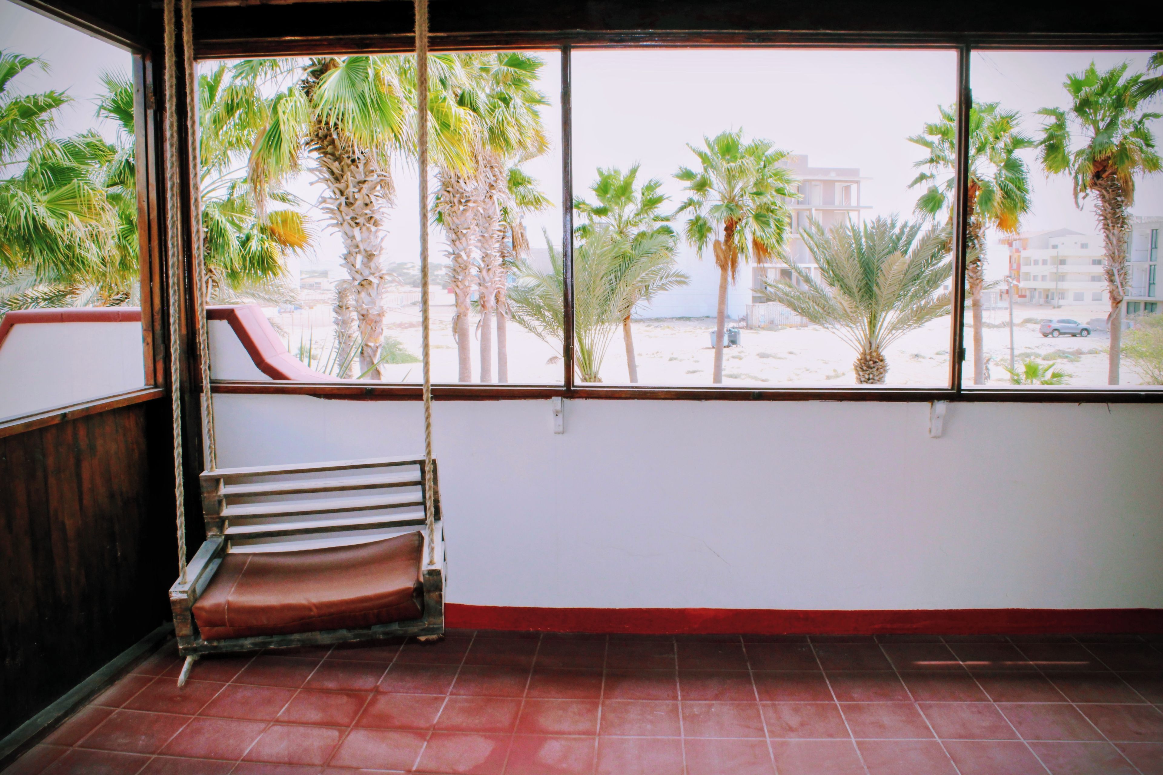 A room with a large window, a red bench, and a view of palm trees and buildings.