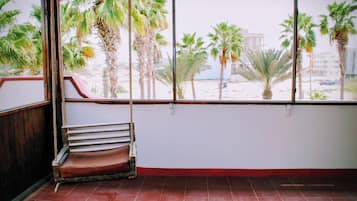 A room with a large window, a red bench, and a view of palm trees and buildings.