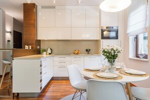 A modern kitchen with white cabinetry, a built-in oven, and a dining area with a round table set for four. - Imperial Apartments - Haffnera Residence (Sopot)