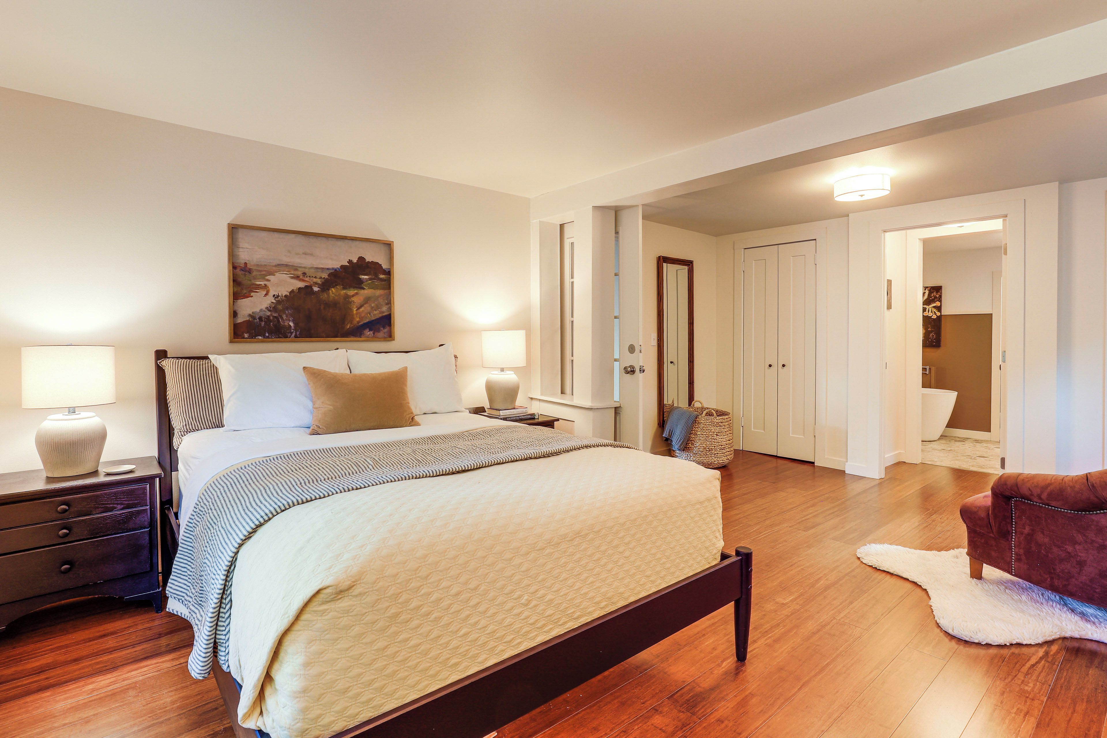 A hotel room with a large bed, bedside lamps, a painting on the wall, and a view of the hallway.