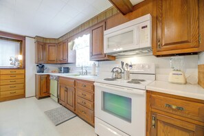 Una cocina con armarios de madera, microondas, estufa y cafetera.