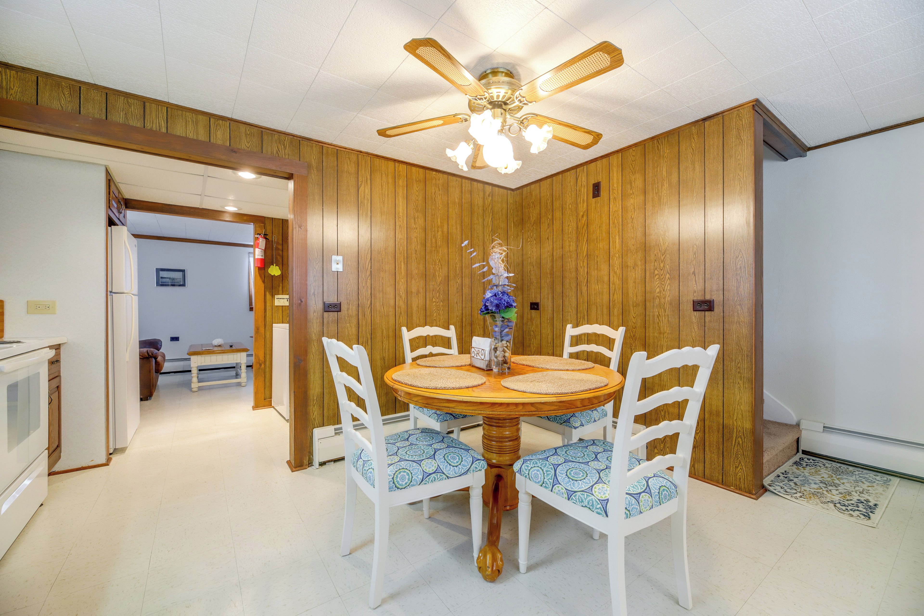 A dining area with a wooden table, white chairs, and a ceiling fan.
