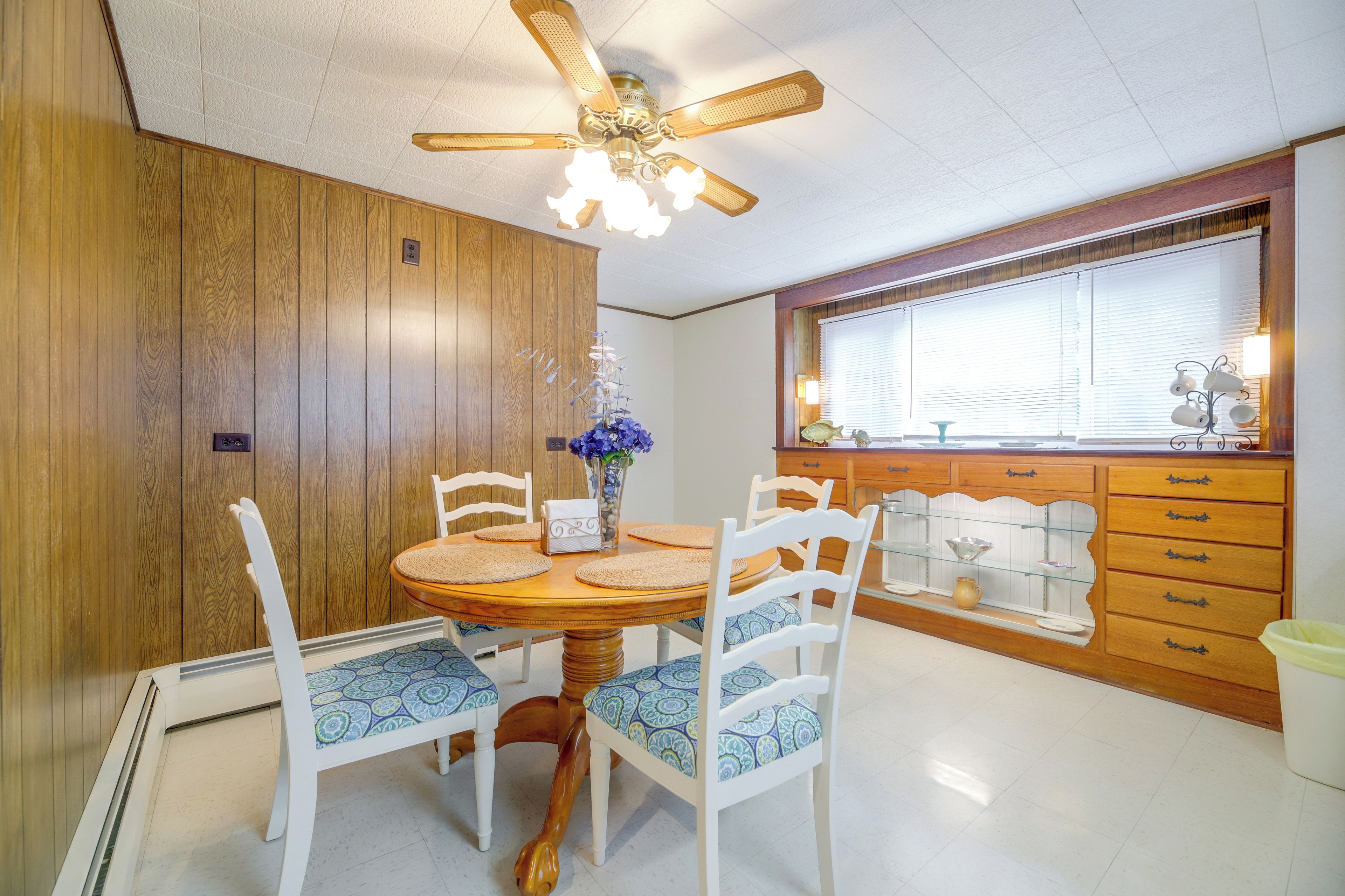 A dining area with a wooden table, white chairs, and a ceiling fan.