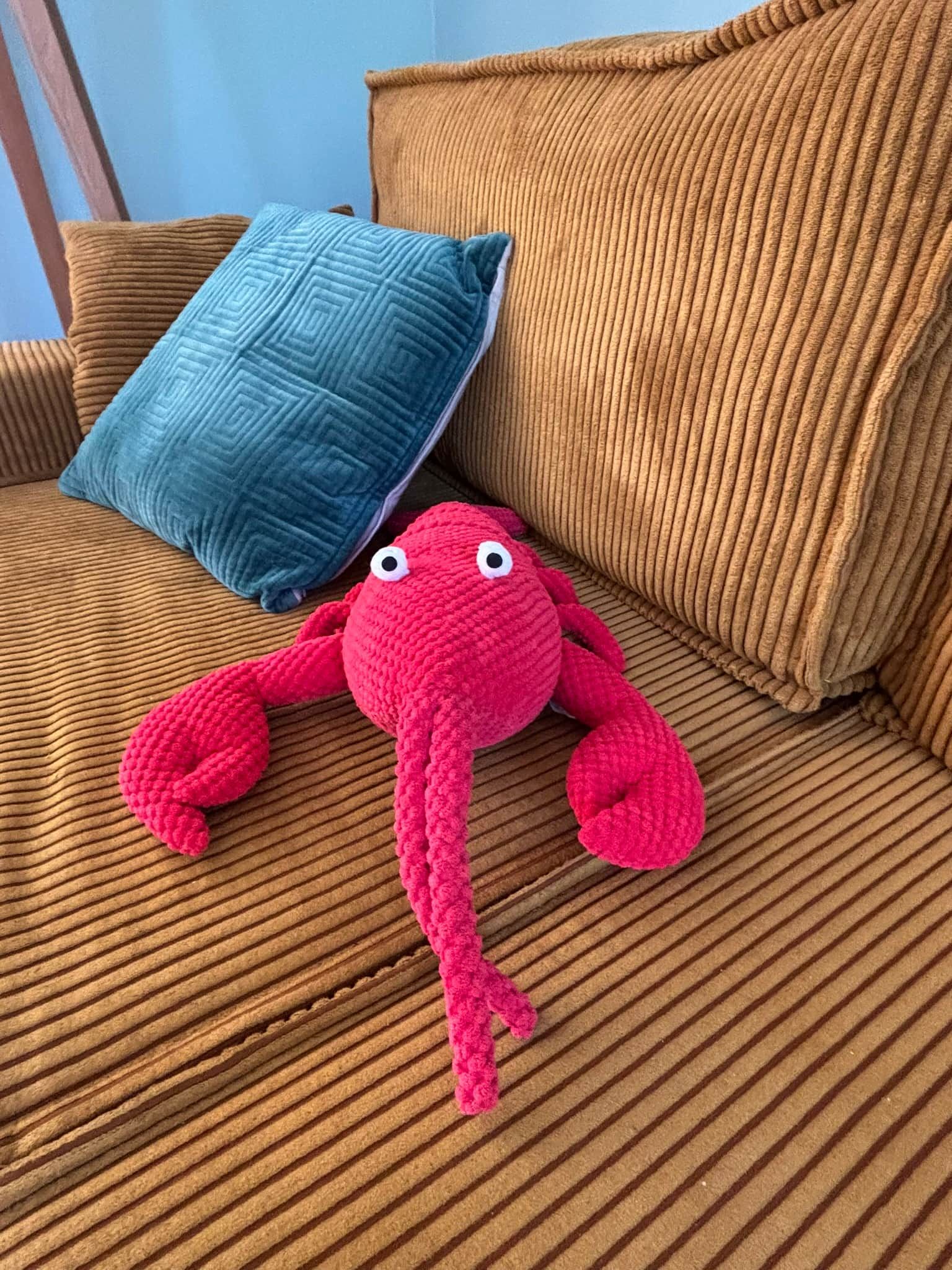Un canapé marron avec un coussin bleu et un jouet en peluche rose.