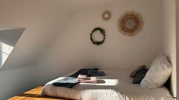 Une chambre avec un plafond en pente, un lit avec des oreillers et une couverture, une table en bois et des éléments de décoration murale, notamment une guirlande et un motif en forme de soleil.