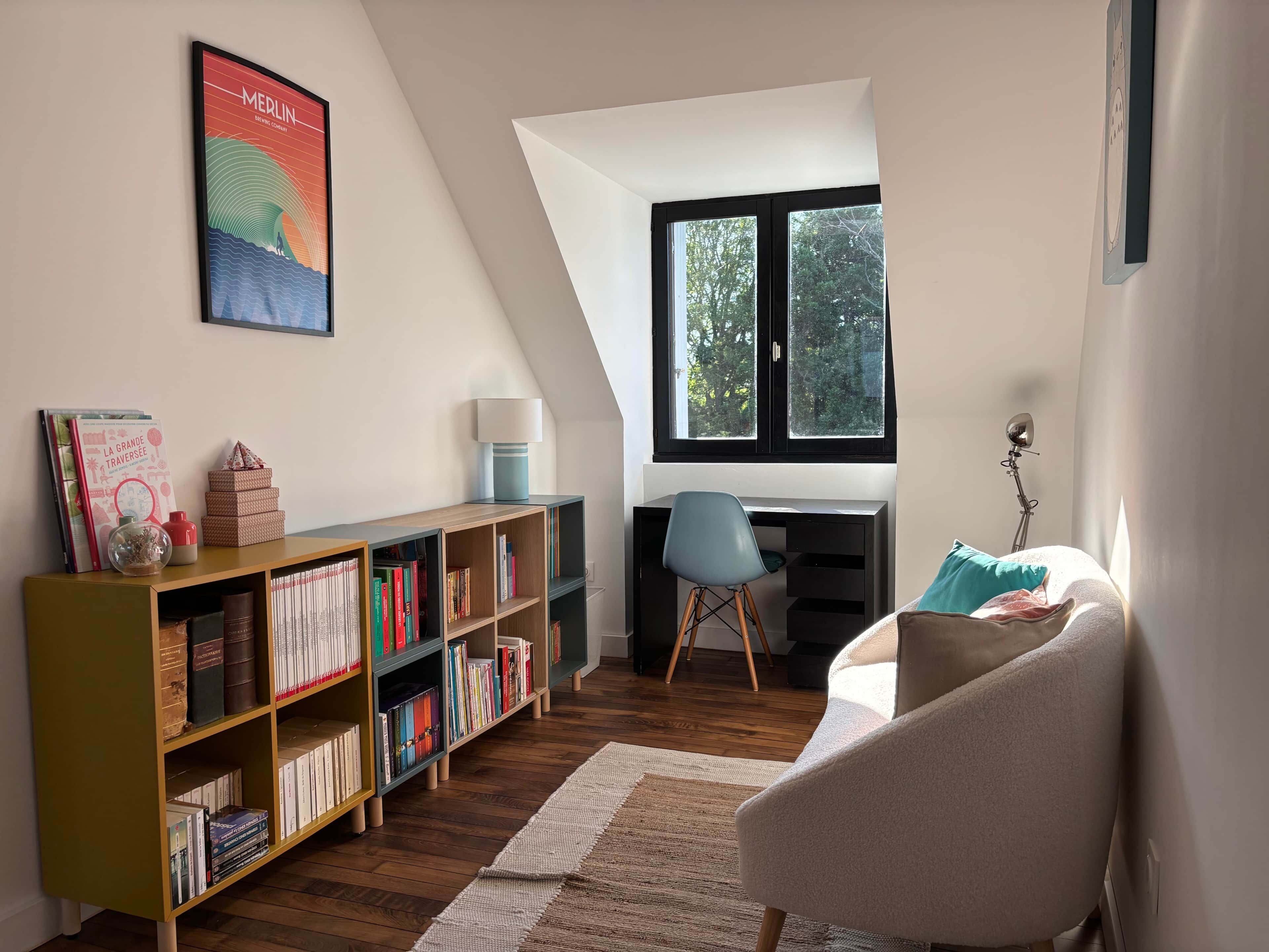 Une pièce comprenant un bureau, une chaise, des étagères et une fenêtre donnant sur des arbres.