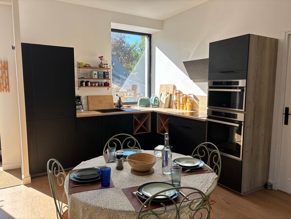 A modern kitchen with a dining area, featuring a built-in oven, a window with a view, and a variety of kitchen utensils and appliances.