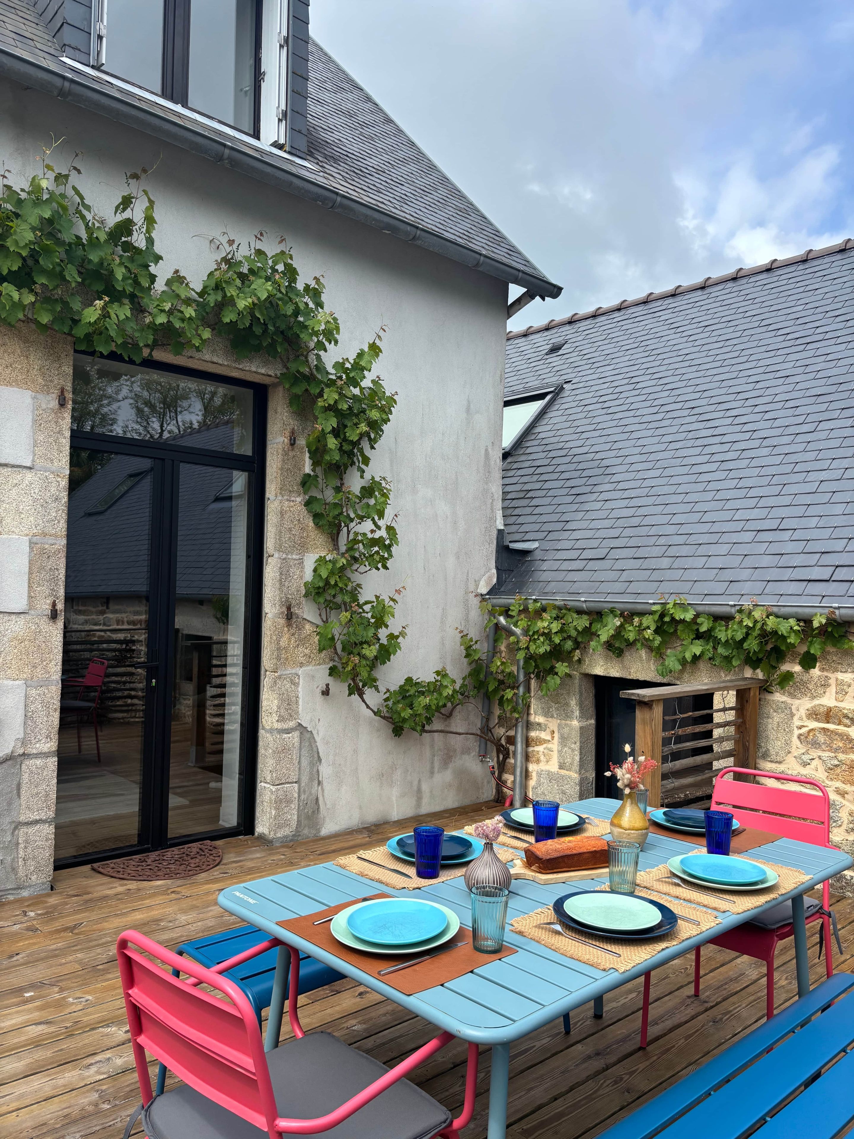 Un espace de restauration en plein air avec une table dressée pour quatre personnes, entouré de murs en pierre et d’une terrasse en bois.