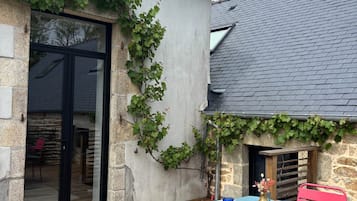 Un espace de restauration en plein air avec une table dressée pour quatre personnes, entouré de murs en pierre et d’une terrasse en bois.