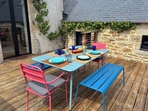 An outdoor dining area with a stone wall, wooden deck, and a table set with blue plates and chairs.