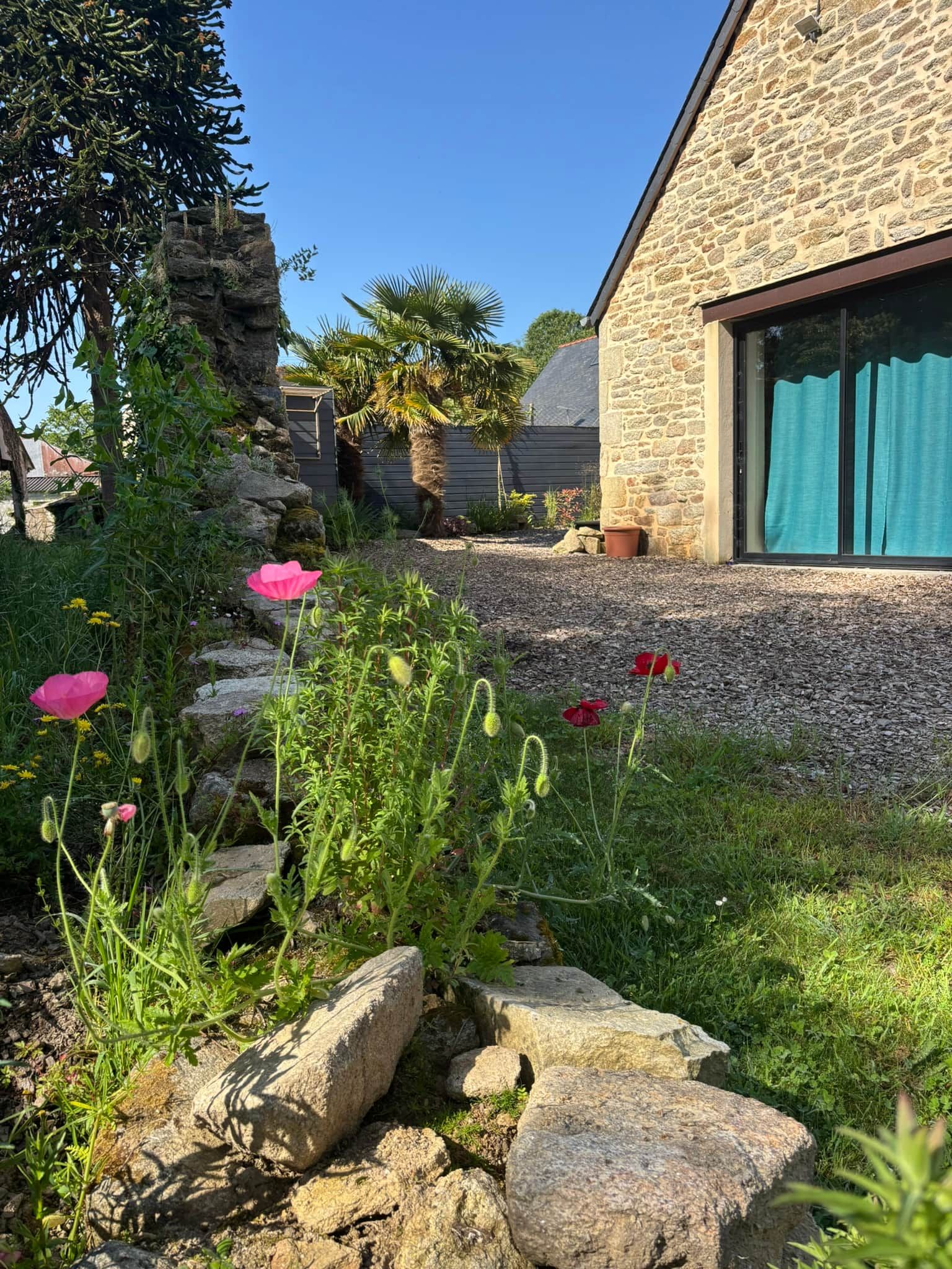 Een gebouw van steen met een modern ontwerp, omgeven door een tuin met verschillende planten en bloemen.