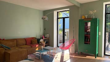 Un salon comprenant un canapé, une table basse, un fauteuil rouge, un meuble vert et une grande fenêtre.