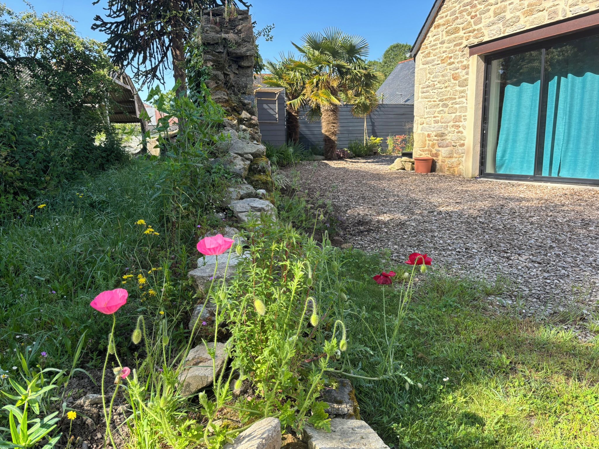 Een tuin met een grindpad dat naar een stenen gebouw met een raam leidt.