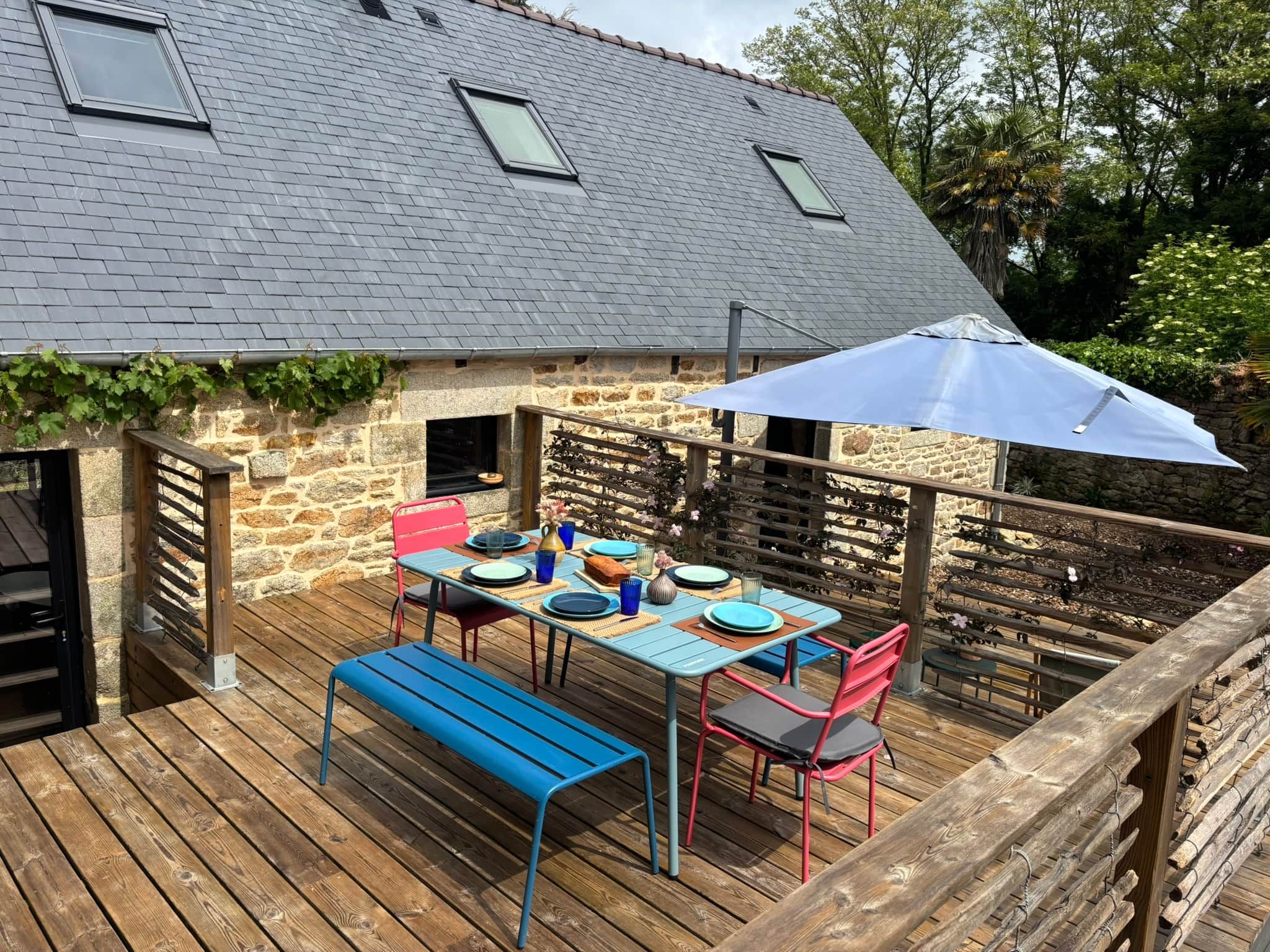 Une terrasse en bois avec une table dressée pour les repas, un banc et un espace abrité avec un parasol.