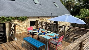 Une terrasse en bois avec une table dressée pour les repas, un banc et un espace abrité avec un parasol.
