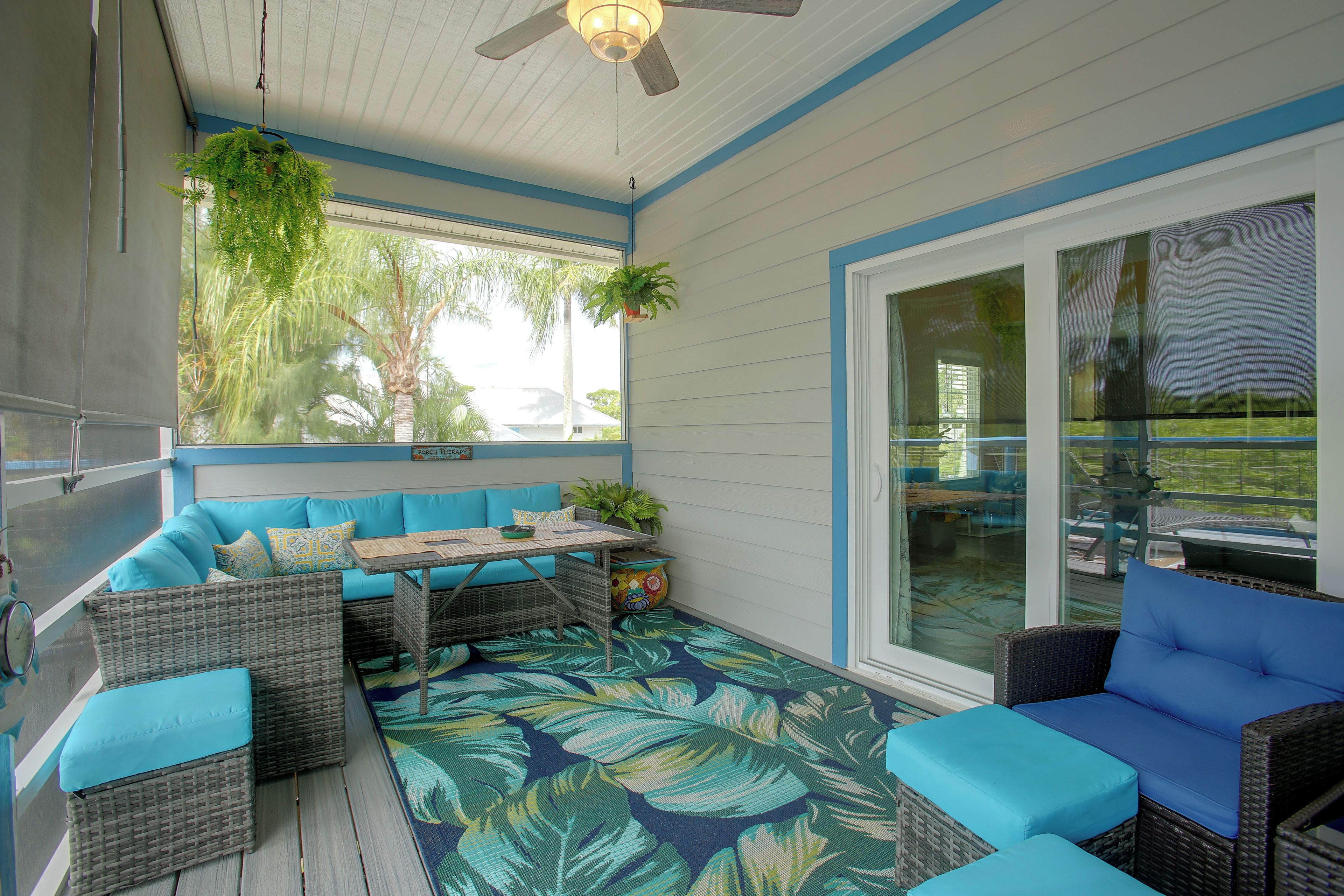 Un espace extérieur abrité, aménagé avec des meubles en osier et un sol orné de motifs de feuilles tropicales.