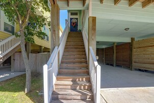 Una escalera de madera que conduce a una puerta con un adorno de ramas, flanqueada por barandas de madera y un árbol.