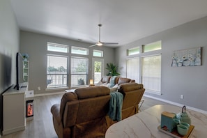 A living room with a brown leather sofa, a ceiling fan, and a dining table with a tray of tea set. - Steps to Sylvan Beach Park! Family Getaway (La Porte)