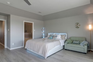 A bedroom with a bed, a nightstand, a chair, a wall-mounted shelf, and a door leading to a bathroom. - Steps to Sylvan Beach Park! Family Getaway (La Porte)