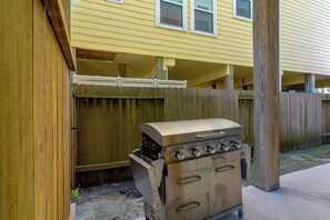 A portable gas grill with four burners and a control panel, positioned in front of a wooden fence with a yellow building in the background. - Steps to Sylvan Beach Park! Family Getaway (La Porte)