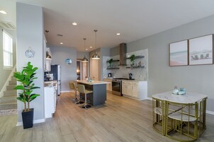 Una cocina moderna con una isla central, iluminación colgante y un comedor con mesa dorada.