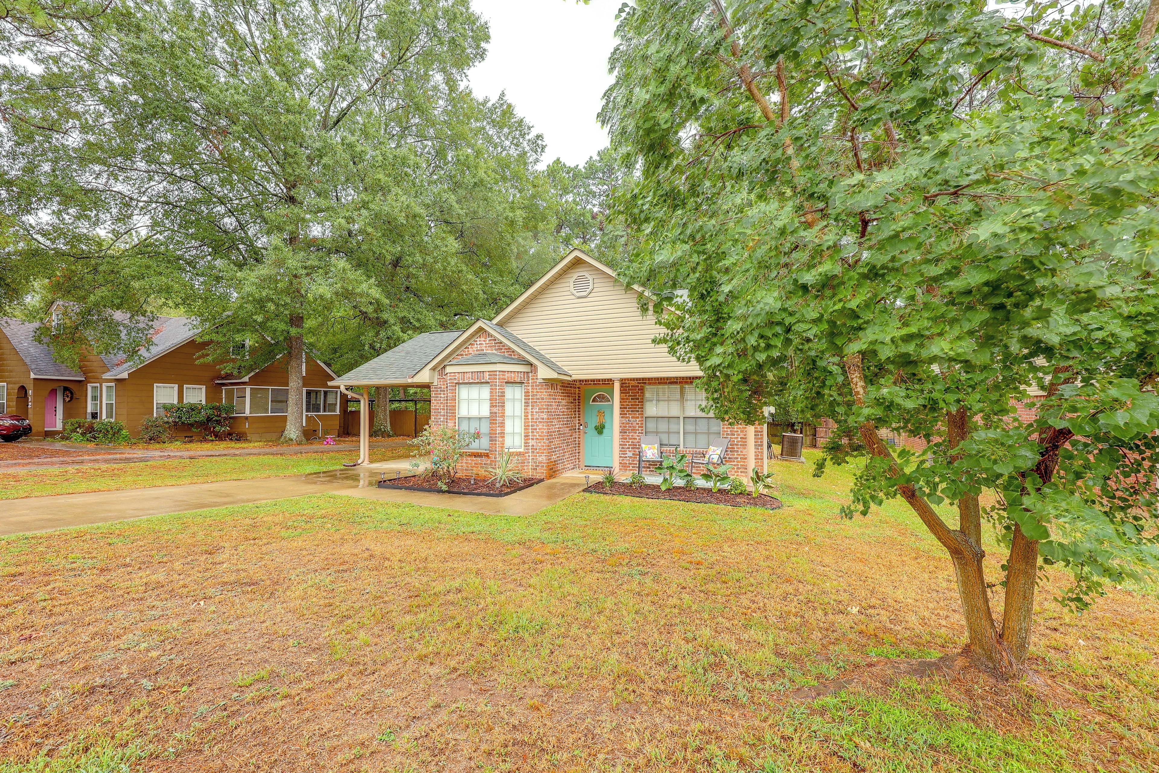 A small brick house with a gabled roof, a front porch with two chairs, and a well-maintained lawn.