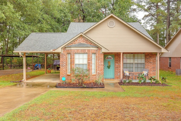 A single-story brick house with a front porch, a covered patio, and a front yard with a small garden.