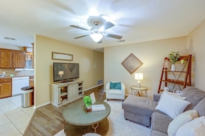 A living room with a television, a ceiling fan, a coffee table, a sofa, and a small table with a lamp.