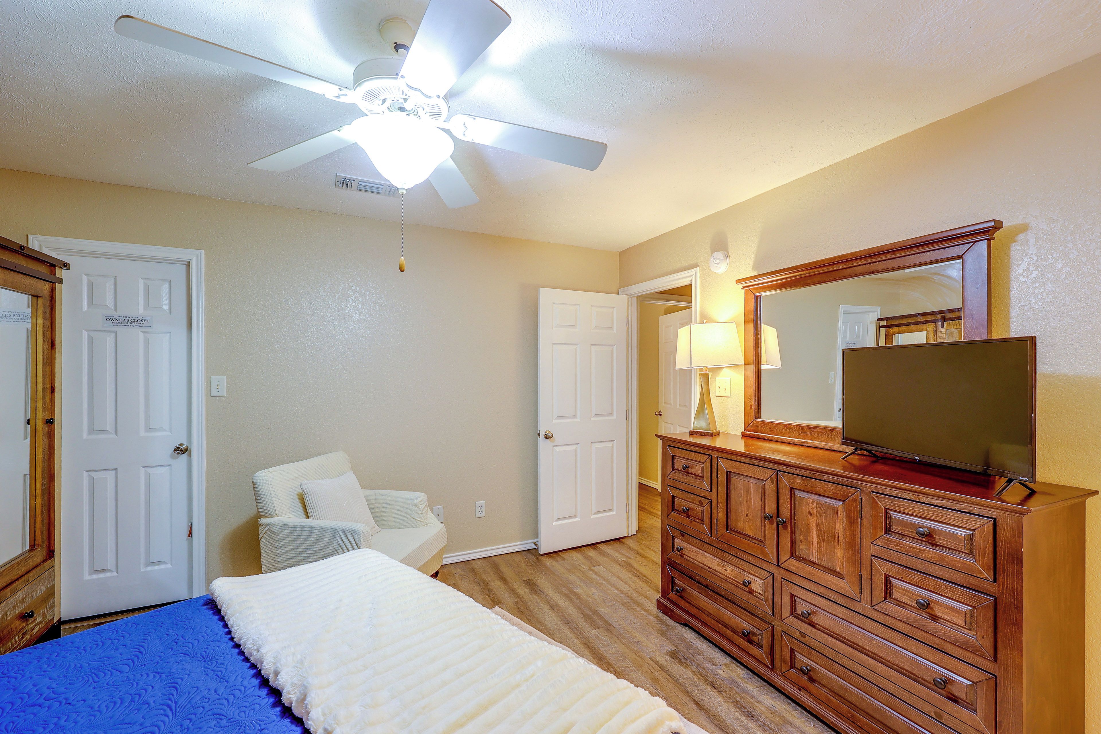 A bedroom with a bed, dresser, mirror, ceiling fan, and two doors.