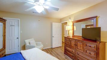 A bedroom with a bed, dresser, mirror, ceiling fan, and two doors.