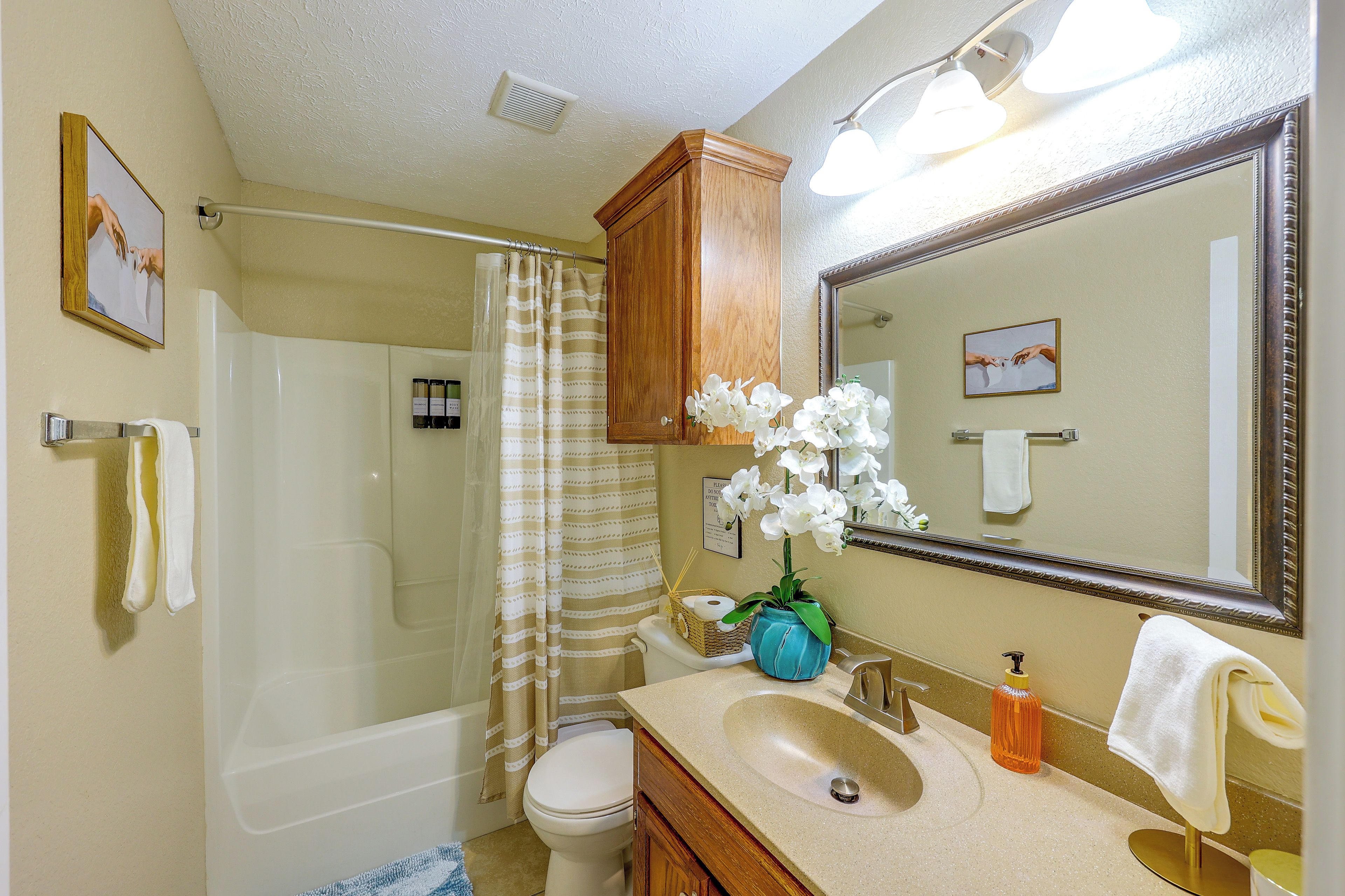 A bathroom with a shower, toilet, sink, and a large mirror.