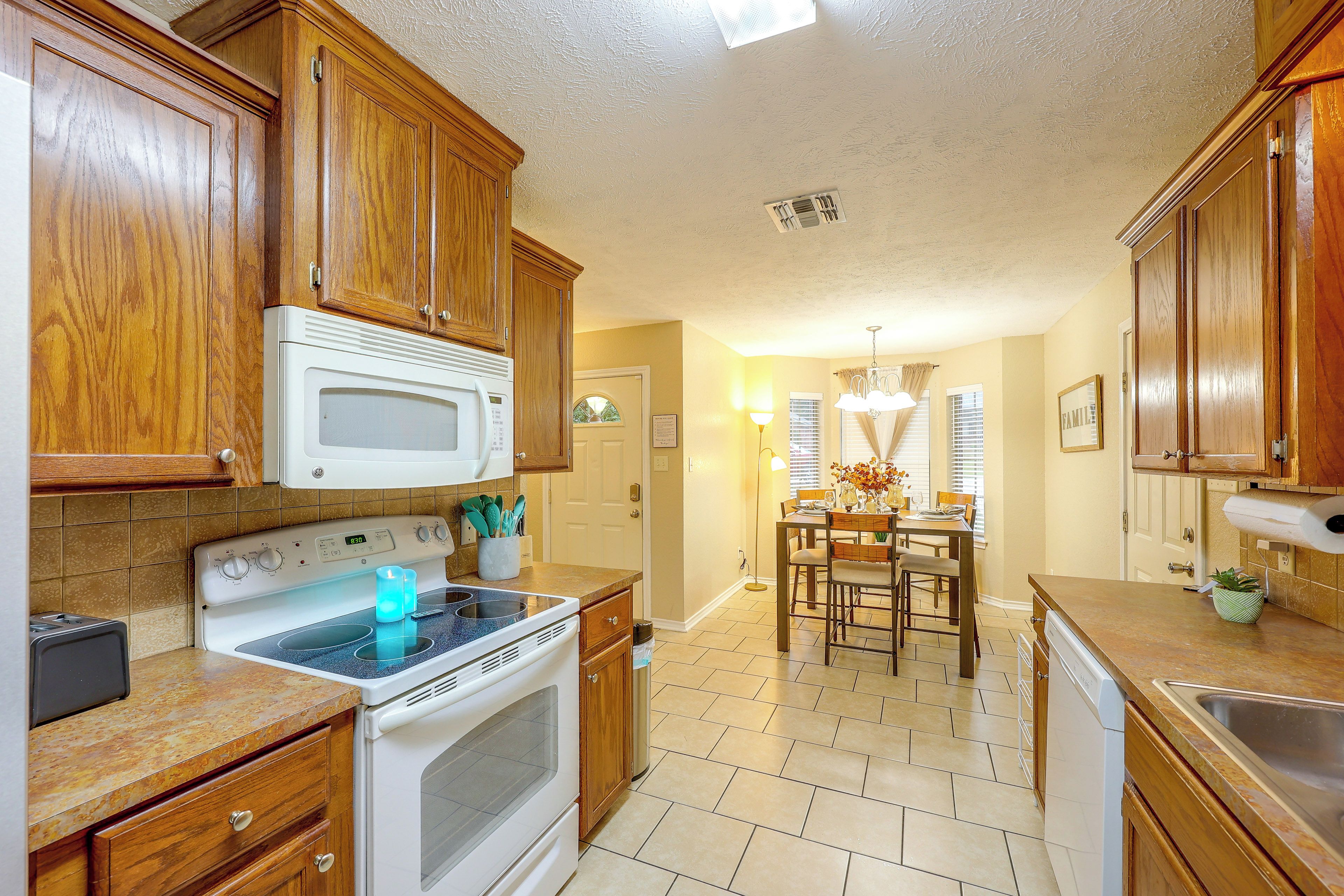 A kitchen with wooden cabinets, a white microwave, an oven, and a dining area with a chandelier.