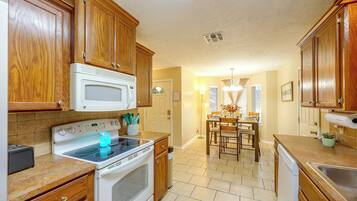 A kitchen with wooden cabinets, a white microwave, an oven, and a dining area with a chandelier.
