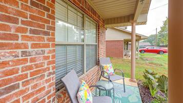 A covered porch with two chairs and a table, a brick wall, and a red car in the background.