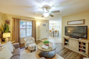 A living room with a ceiling fan, a television, a dining area, and a door leading to another room.