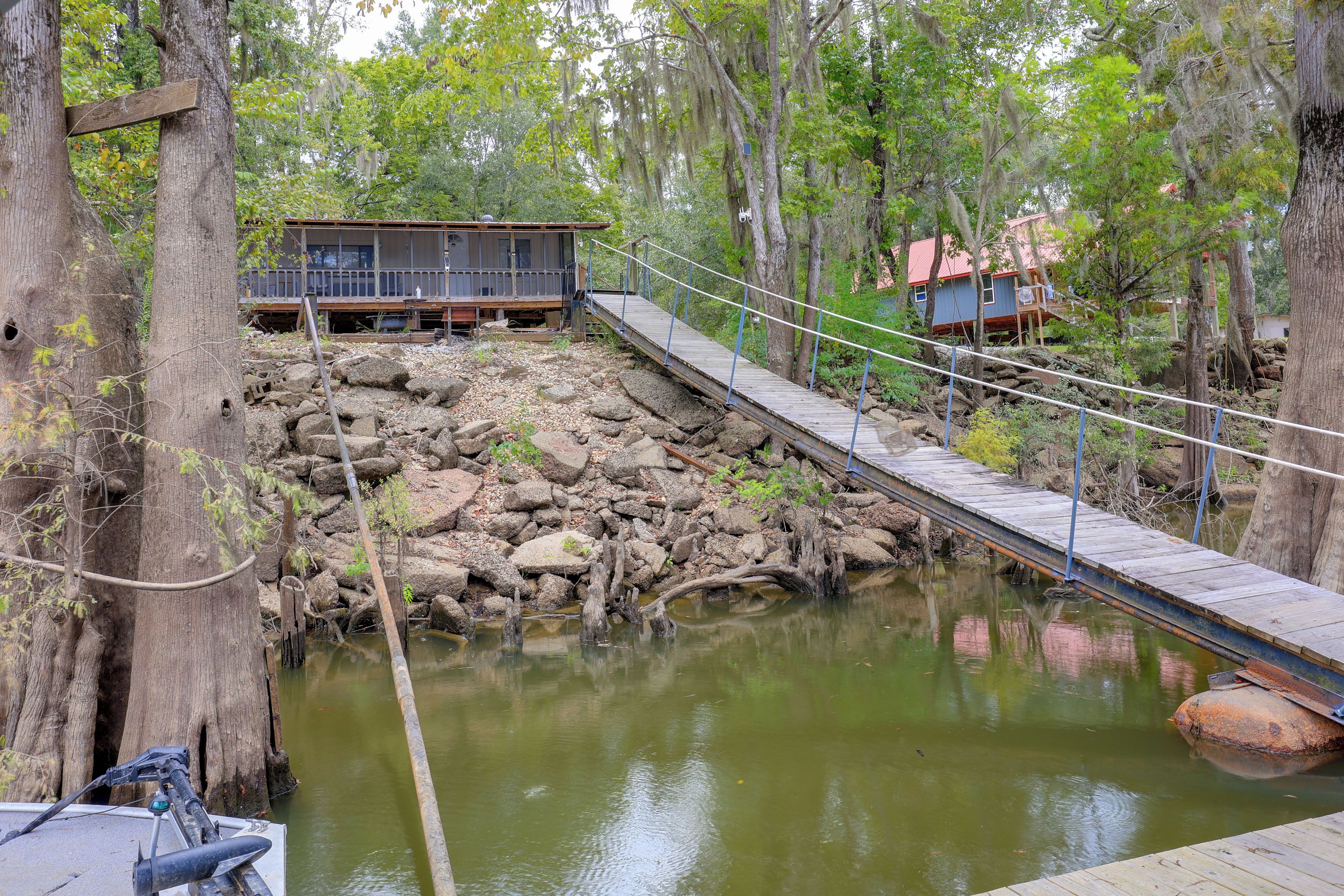 A rustic wooden bridge over a rocky water body, leading to a cabin with a deck.