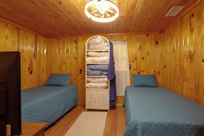A room with two beds, a wooden ceiling, a ceiling light, a white cabinet, and a television.