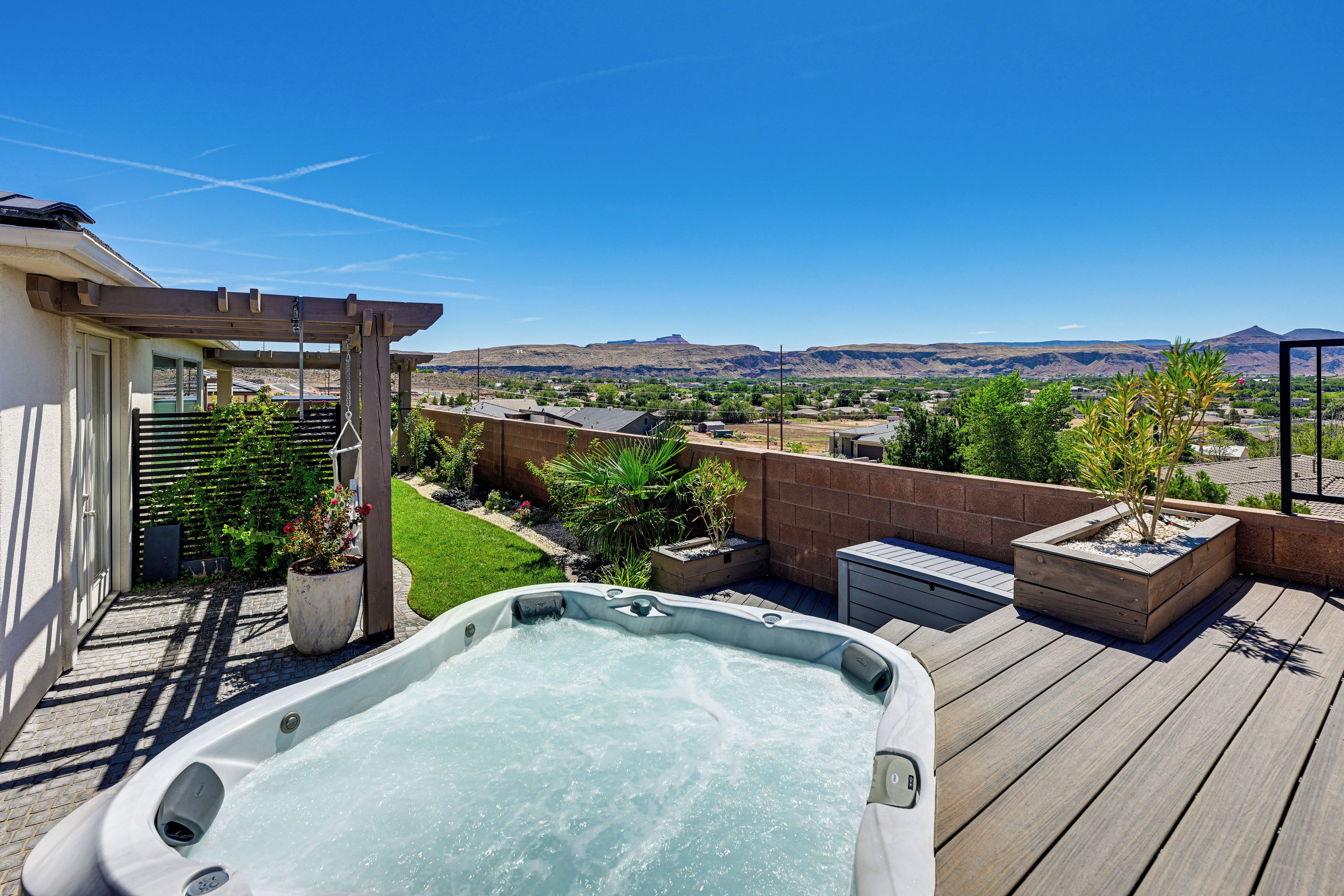 A hot tub on a wooden deck with a view of a residential area and mountains in the distance.