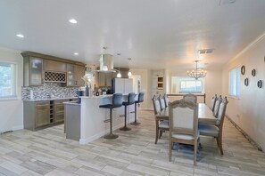 A spacious kitchen with modern appliances, a dining area with a wooden table and chairs, and a chandelier. - Half-acre Yard, Modern Interior! Aurora Home (Aurora)