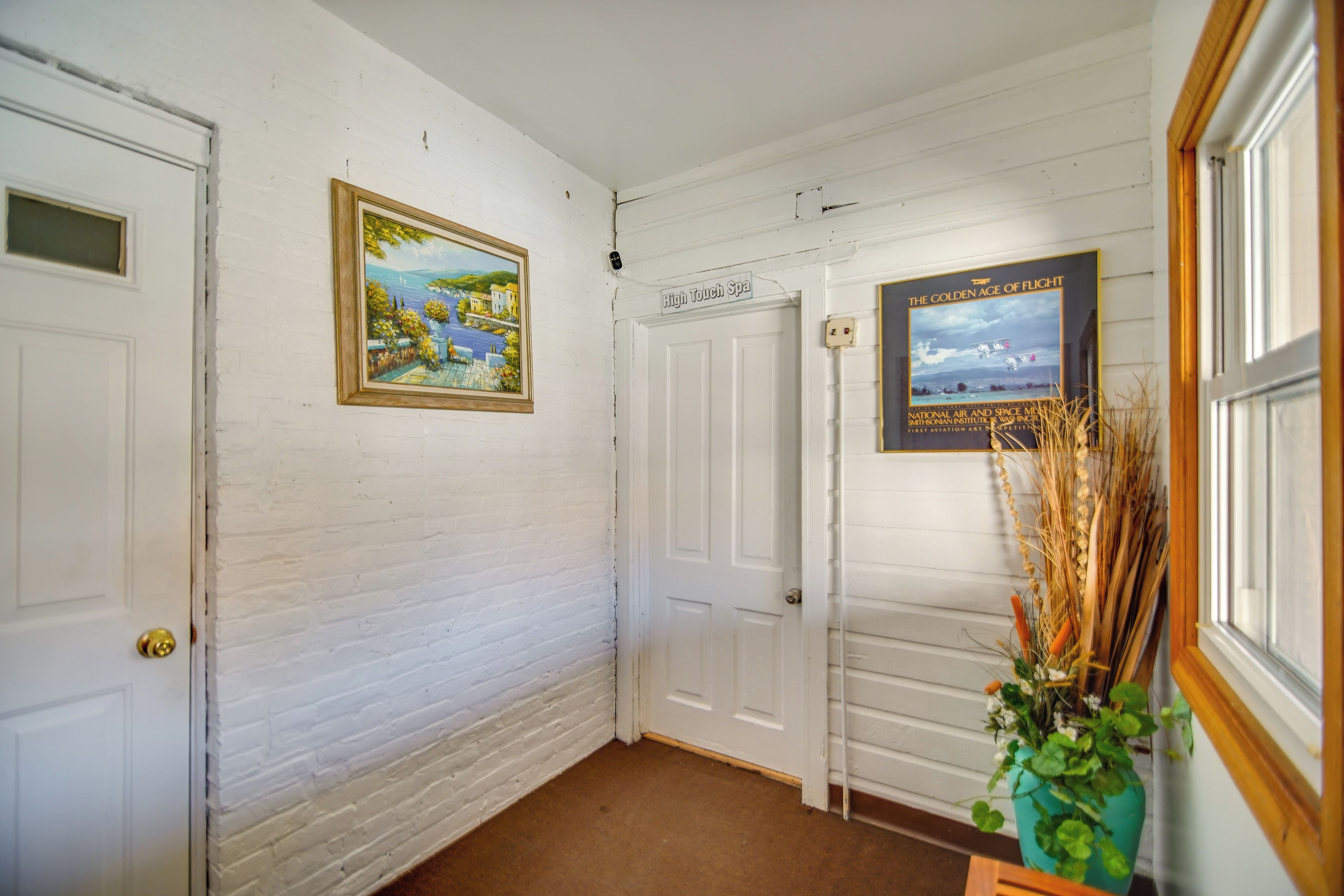 A hallway with white walls, a door labeled 'High Touch Spa,' and two framed pictures.