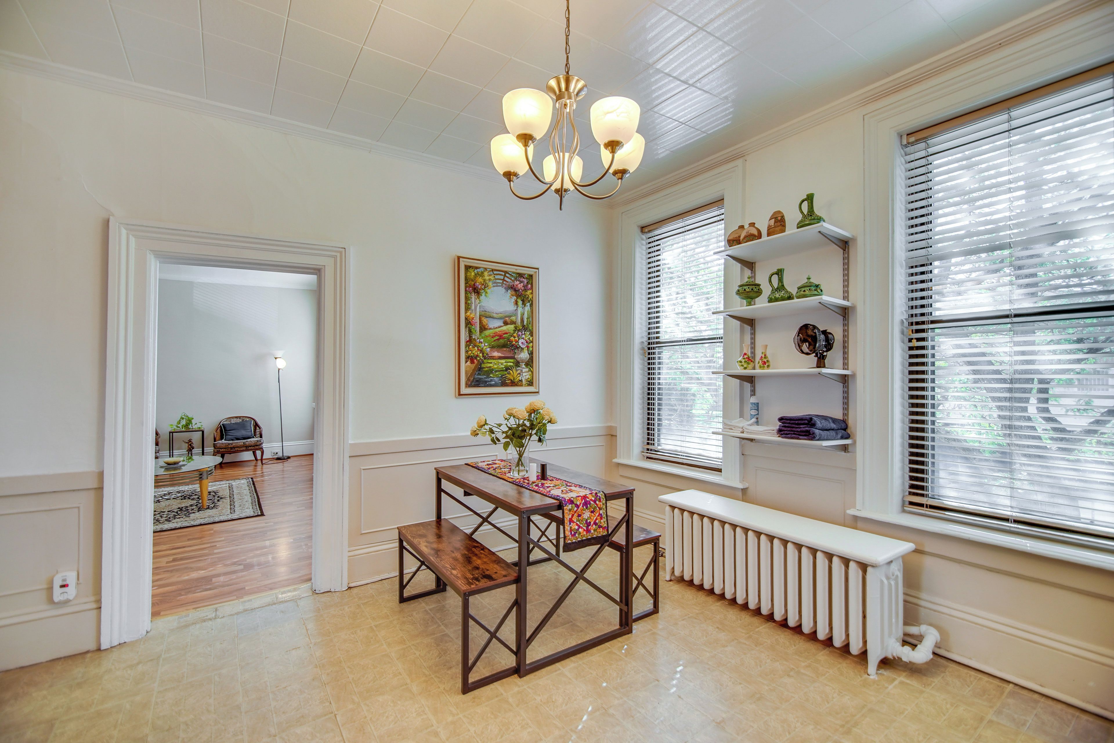 Una habitación con mesa de comedor, radiador, candelabro y ventana con persianas.