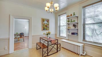 Una habitación con mesa de comedor, radiador, candelabro y ventana con persianas.