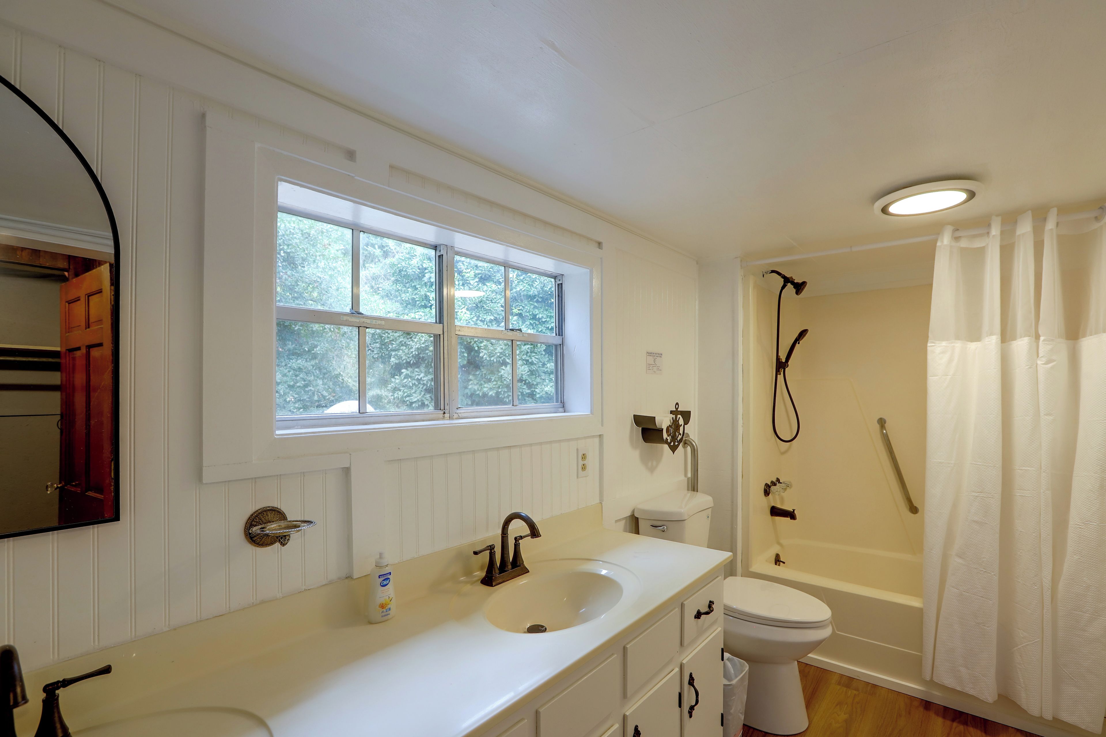 A bathroom with a window, a sink, a toilet, and a shower.