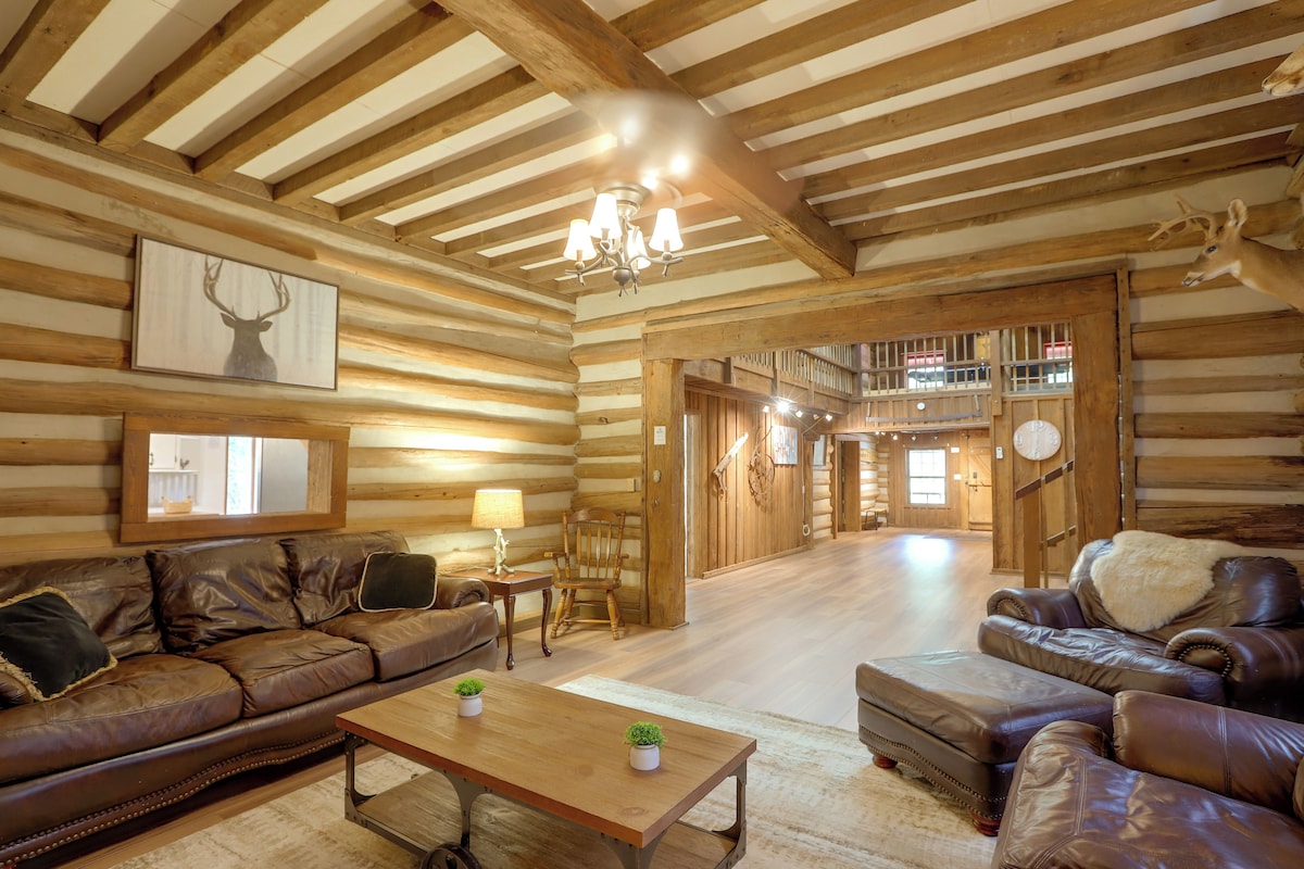 A log cabin interior with a wooden ceiling, leather sofas, a wooden coffee table, and a chandelier.