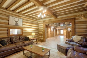 A log cabin interior with a wooden ceiling, leather sofas, a wooden coffee table, and a chandelier.