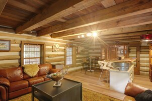 A log cabin interior with a leather sofa, a coffee table, a dining area with chairs, and a kitchen area with a sink and counter.