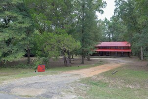 Un edificio rústico con techo rojo, rodeado de árboles frondosos y un camino de grava que conduce a él.