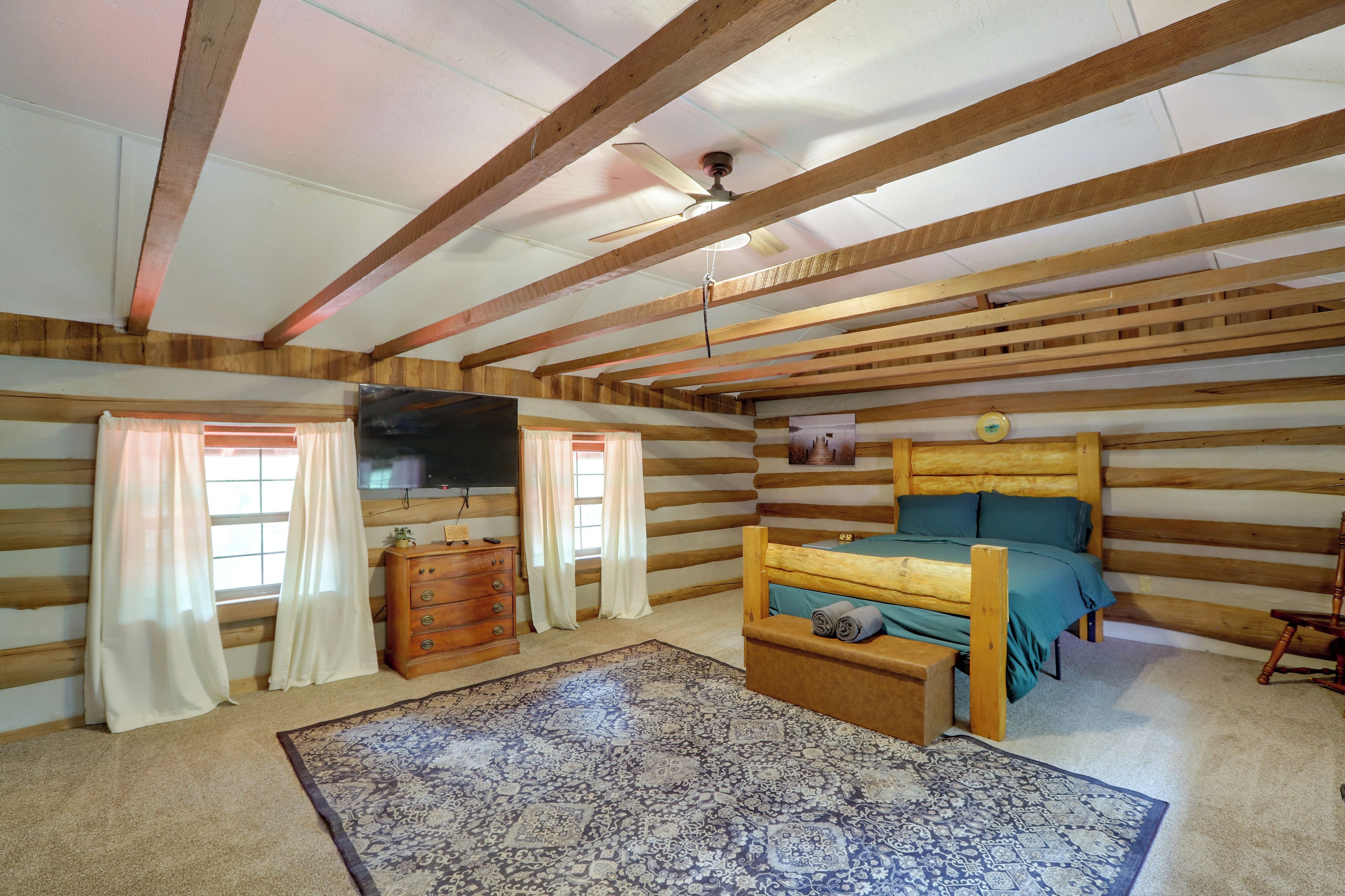 A log cabin room with a bunk bed, wooden beams, a ceiling fan, a dresser, and a patterned rug.